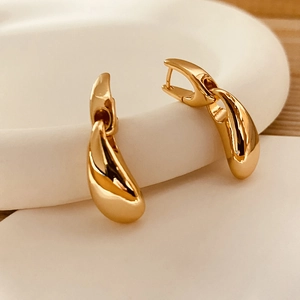 Polished gold teardrop hoop earrings with high-gloss finish on a minimalist tray