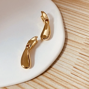 Detail showing high-polished golden teardrop huggie earrings on a ceramic dish