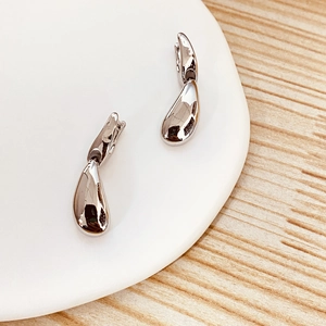 Macro detail of high-polished silver water drop earrings on a ceramic display