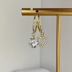 Detail of gold double-hoop earrings featuring a faceted zircon and micro-pave heart charm