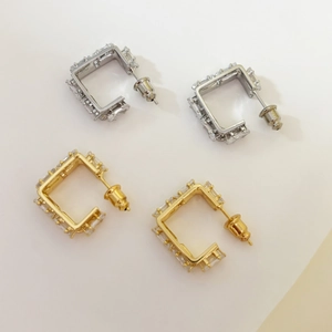 Close-up of gold and silver rectangular geometric earrings with micro-set zircon stones