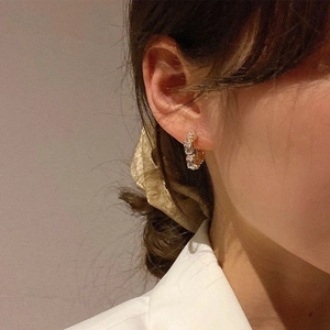 Close-up of golden geometric earrings with rectangular zircons on model's ear