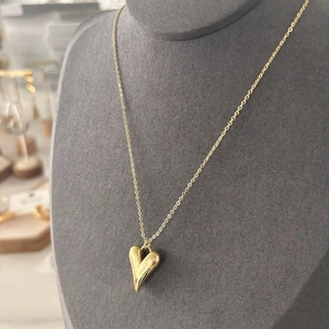 Vue macro d'un collier pendentif cœur 3D plaqué or 18 carats sur un support gris