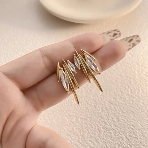 Gold wing earrings with marquise zircon stones and sharp metal spikes in a hand