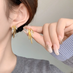 Detail of gold metal fringe earrings with marquise-cut zircons worn on model ear