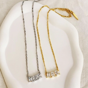 Colliers dorés et argentés avec pendentifs à trois zircons sur un plateau en céramique
