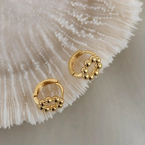Dettaglio di orecchini a cerchio geometrici placcati oro 18K su corallo bianco