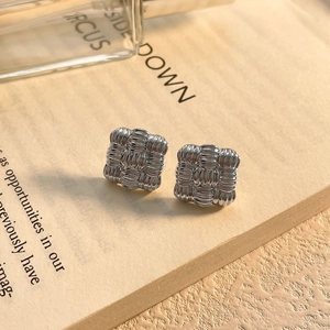 Close-up of square silver stud earrings with a woven texture on a vintage book page