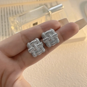 Close-up of silver geometric square earrings with a textured woven pattern finish