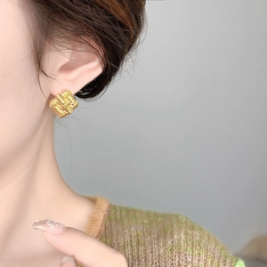 Macro view of gold-plated geometric square earrings with a textured woven pattern