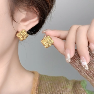 Close-up of gold-plated square stud earrings featuring a delicate woven metal texture