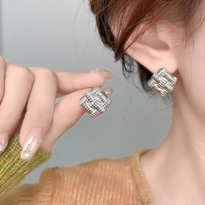 Macro detail of geometric silver woven square stud earrings on a fashion model