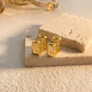 Close-up of gold-plated square zircon earrings on natural stone for luxury aesthetic