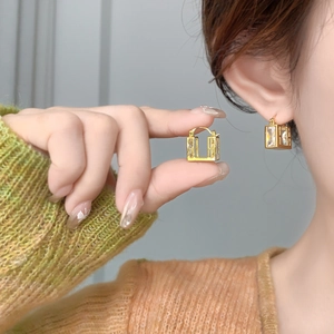 Macro detail of gold square zircon earrings showing the geometric frame and clear crystal