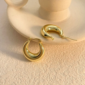Detail of high-polished 18K gold-plated C-shape hoop earrings on a ceramic base