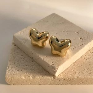Macro shot of 18K gold plated bow earrings on stone props showing shiny metallic texture