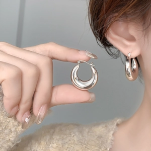 Macro detail of high-polished silver hoop earrings with secure clasp on a female model