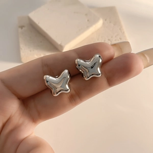 Close-up of hollow butterfly stud earrings with silver mirror finish on stone background