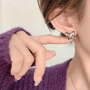 Detailed view of silver liquid heart earrings in hollow design on model wearing a sweater