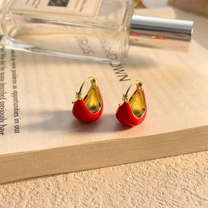 Détail de boucles d'oreilles en émail rouge en forme de U posées sur un livre ouvert