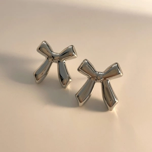 Macro view of mirror polished silver bow stud earrings on minimalist cream background
