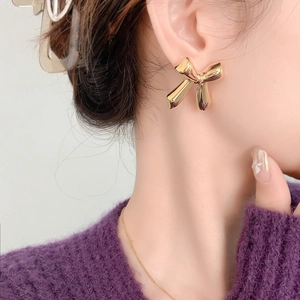 Close-up of golden bow-shaped stud earrings worn by a model in a purple knit sweater