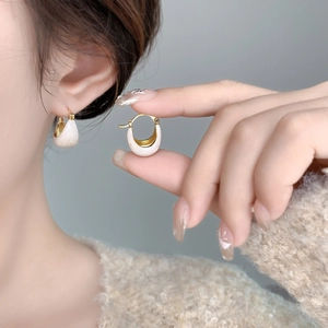 Détail de boucles d'oreilles en U dorées avec émail crème pour un look très élégant
