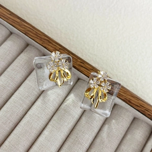 Macro shot of zircon flower and gold bow stud earrings on grey velvet jewelry box