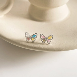 Macro shot of silver butterfly stud earrings with colorful zircon inlay and hollow wings
