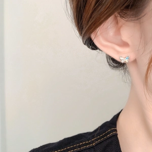 Mini silver butterfly stud earrings with blue enamel wings shown on a model's ear