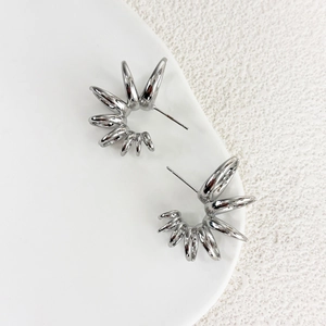 Detailed view of silver sunburst earrings with a polished finish on a white surface