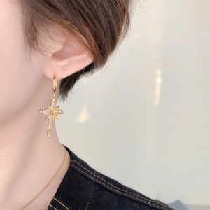 Close-up of elegant gold cross star earrings with zircons on model ear