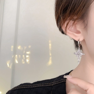 Close-up of a model wearing a silver star-cross earring with sparkling zircon tassel detail