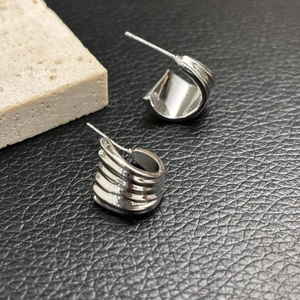 Macro shot of silver C-shaped earrings with layered fan texture on black leather background