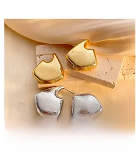 Close-up of geometric hollow earrings with hammered texture on silk and marble