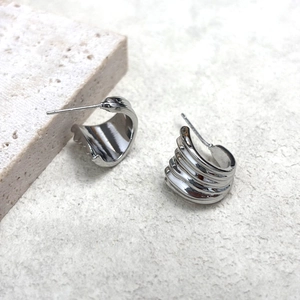 Polished silver geometric fan texture earrings on a minimalist stone display stand