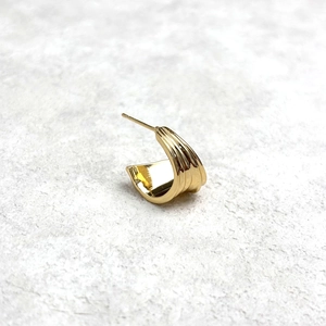 Detailed view of C-shaped gold earrings with vertical ribbed texture and polished finish