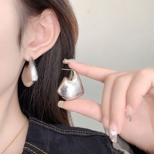 Close-up of geometric irregular silver earrings with hammered metal texture on model