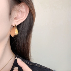 Close-up of polished gold teardrop earring worn by a model showcasing high-shine metal