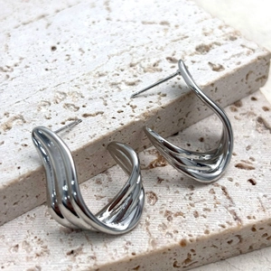 Detailed view of 18K gold plated wavy ribbon earrings on natural travertine stone