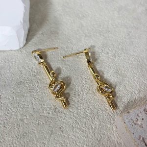 Detailed view of long vintage gold-plated earrings with serpent staff and zircon inlay
