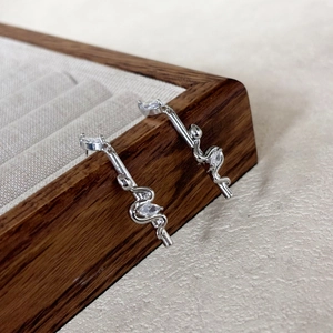 Close-up of silver snake earrings with white marquise zircons on a wooden jewelry box