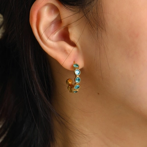 Gros plan de boucles d'oreilles créoles dorées avec cristaux bleus sur mannequin