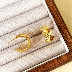 Gold-plated geometric C-shaped hoop and textured disc drop earrings on velvet display