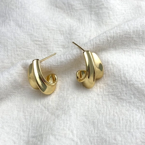 Elegant gold crescent wave stud earrings with minimalist polished texture on white linen