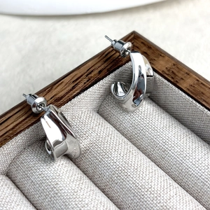 Detailed close-up of polished silver C-shaped stud earrings in a linen jewelry box