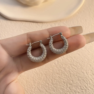 Macro shot of silver-plated hoop earrings with micro-set zircons held by hand