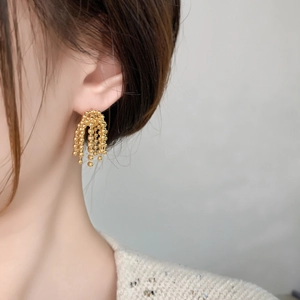 Vue détaillée des boucles d'oreilles à pompons perlés dorés portées par un mannequin
