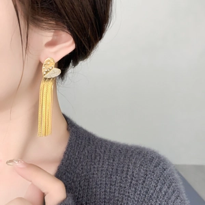 Detail of long gold tassel earrings with heart-shaped studs on model for elegant look