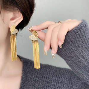 Macro detail of gold tassel earrings with double heart stud and sparkling pavé crystals